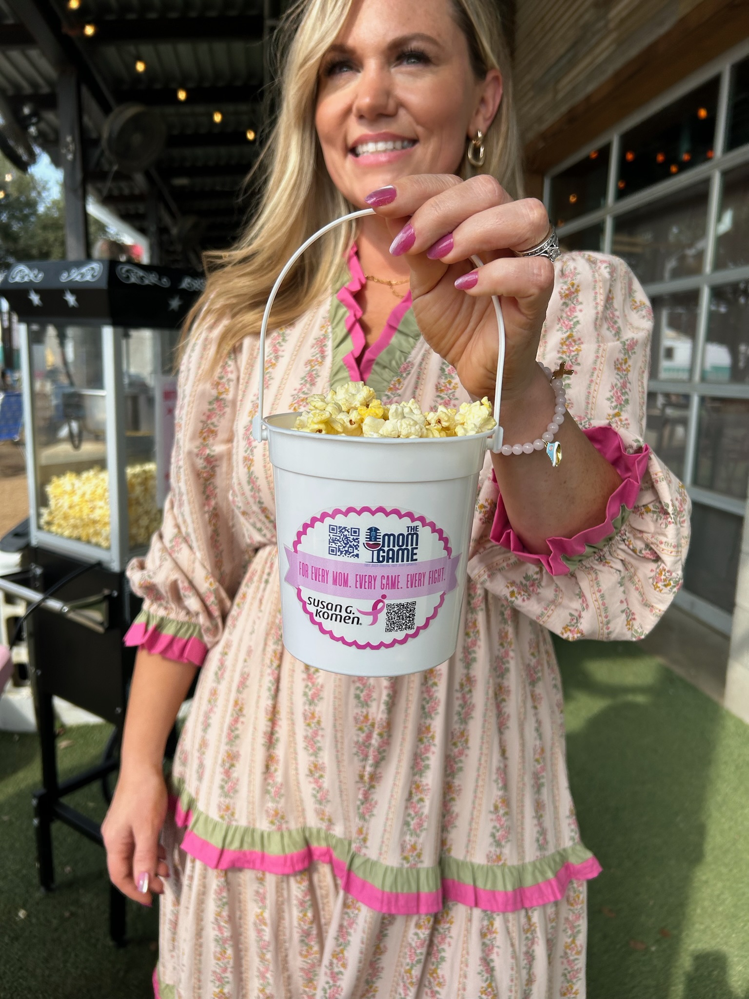 Audrie Dollins holding pink popcorn buckets from The Mom Game Live event at Truck Yard Fort Worth, created to support Susan G. Komen with all proceeds donated to breast cancer awareness.