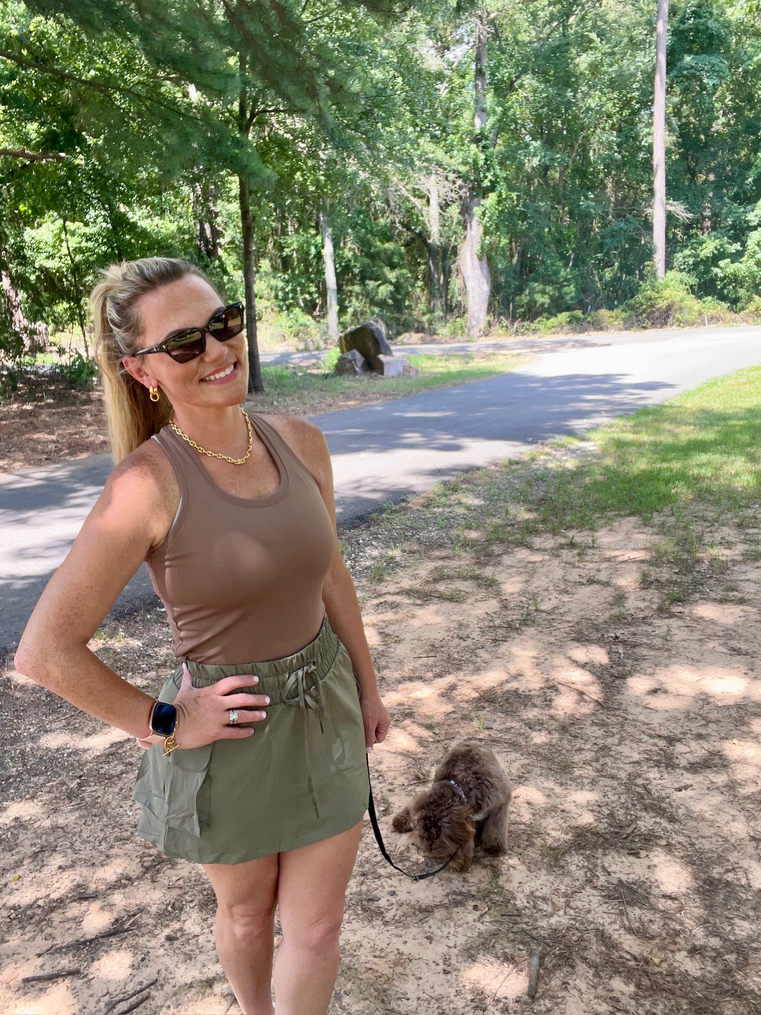Woman modeling a brown sleeveless athletic tank top with an olive green cargo skort in a shaded park, highlighting an easy summer outfit for walking, errands, and casual weekends.