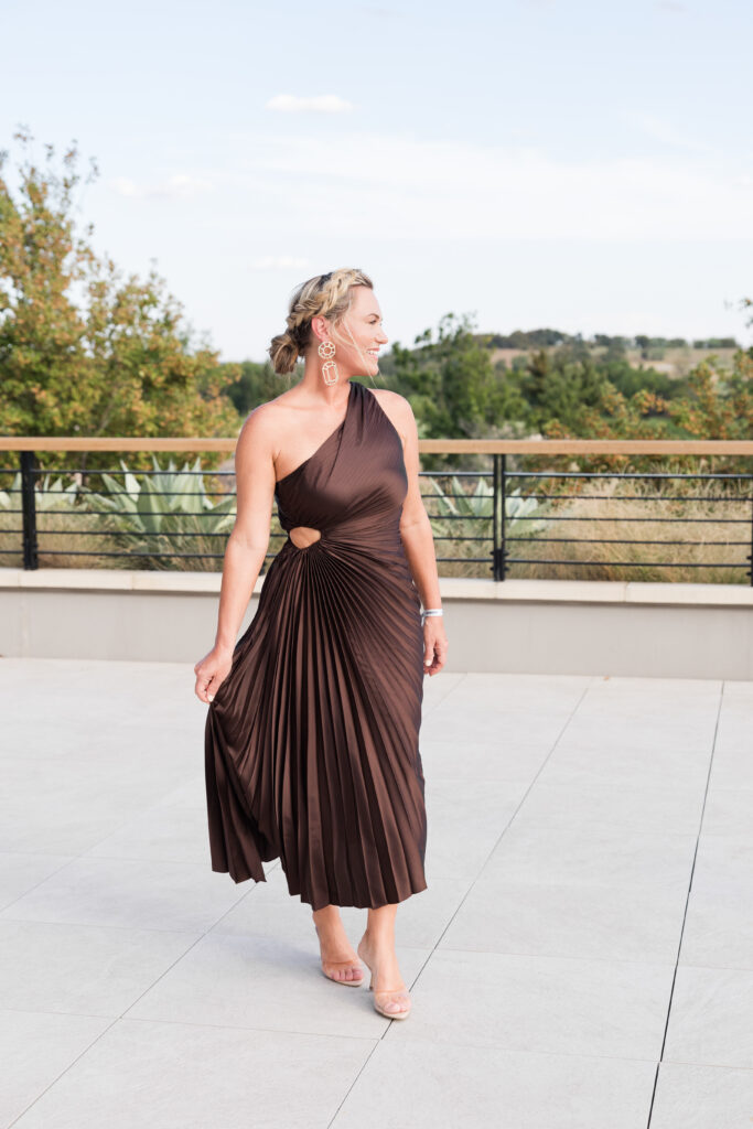Audrie Dollins wearing a brown one-shoulder dress with statement earrings at LTKCon 2026 in Frisco, Texas, sharing her event style as a business owner and influencer management agency founder.