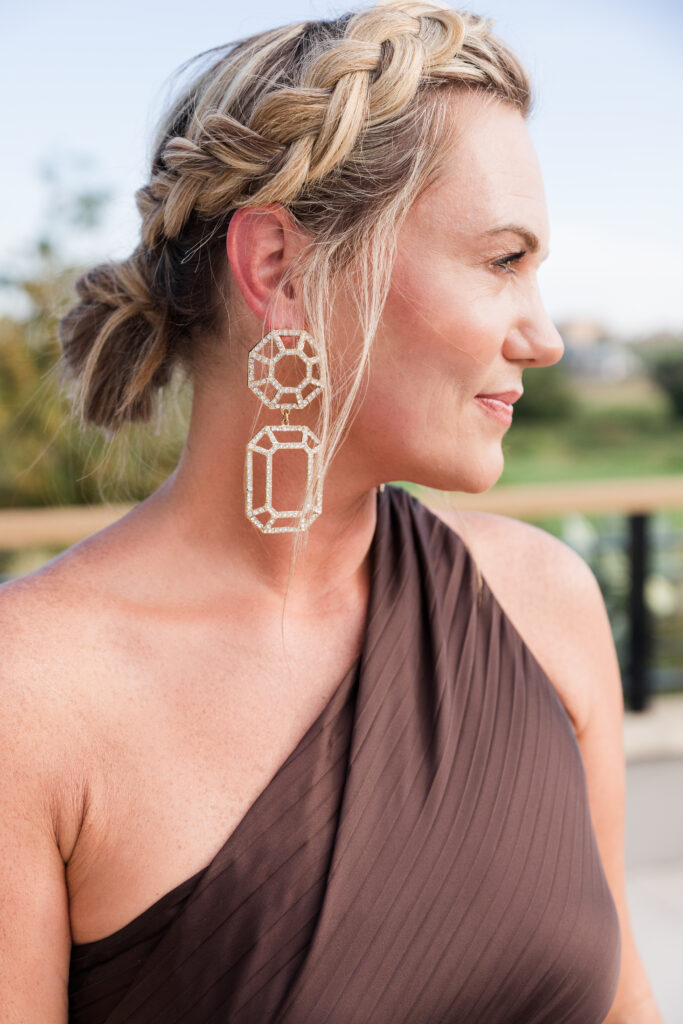 Audrie Dollins wearing a brown one-shoulder dress with statement earrings at LTKCon 2026 in Frisco, Texas, sharing her event style as a business owner and influencer management agency founder.