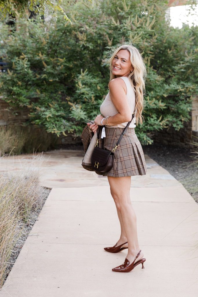 Audrie Dollins wearing a plaid mini skirt, sleeveless top, and woven handbag at LTKCon 2026 in Frisco, Texas, sharing conference fashion as an entrepreneur and influencer management agency founder.